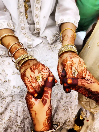 A close-up of hands, showing the rich color of the henna stain against the beautiful white outfits.