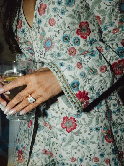 A close-up on the bride's hand, showcasing her stunning engagement ring and the beautiful floral fabric of her outfit.