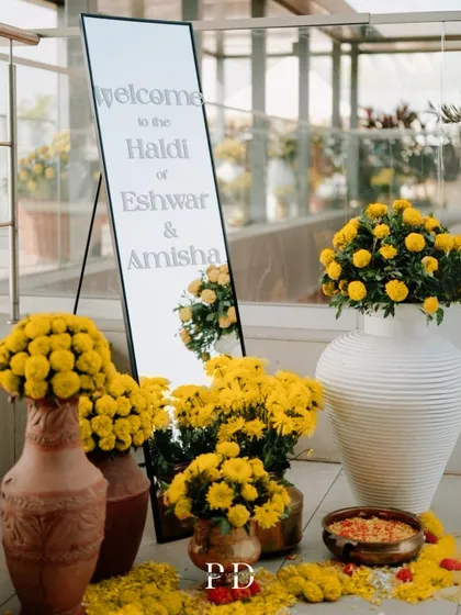 The welcome setup for a modern Haldi, featuring a sleek mirror sign and an abundance of fresh marigolds in contemporary white and terracotta vases.
