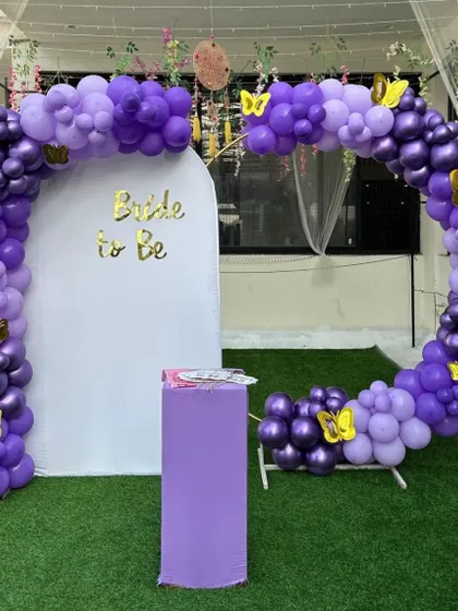 A cute 'Bride to be' photo corner with a purple balloon arch accented with golden butterflies, perfect for a fun bachelorette party.