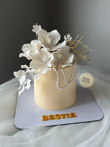 An elegant floral cake with handcrafted, edible fondant flowers. The white flowers and pearls create a classic and sophisticated look.