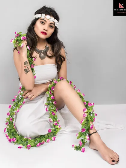 A seated portrait from the 'Gaia' series. The model is dressed in white with a floral garland, looking directly at the camera with a powerful yet gentle expression, capturing the essence of a mythical goddess.