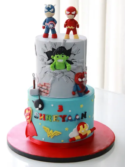 A superhero spectacular for a 3rd birthday! This two-tiered cake is packed with action, featuring the Hulk smashing through a wall, Spider-Man, Captain America, and other hero logos.