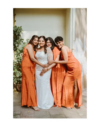 The bride surrounded by her bridesmaids in matching orange dresses. This photo captures the beauty and support of the bridal party.