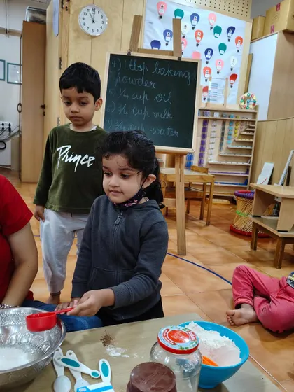 Following the recipe written on the board, a child measures an ingredient. This activity integrates reading, observation, and mathematical concepts in a practical way.