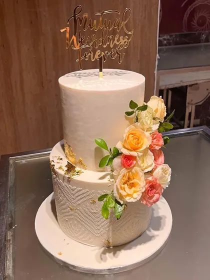 A snapshot of this two-tier beauty right before it went to the venue. The bottom tier has a modern geometric pattern, while the top is smooth, both adorned with a cascade of fresh flowers and a funny "Mutual Weirdness Forever" topper.