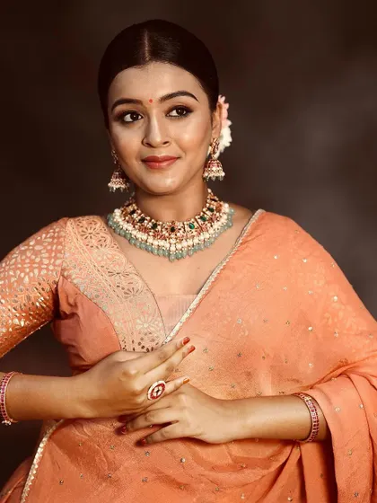 A closer look at the peach lehenga, showing the subtle texture of the fabric and how it pairs with delicate jewelry for a soft, romantic look.