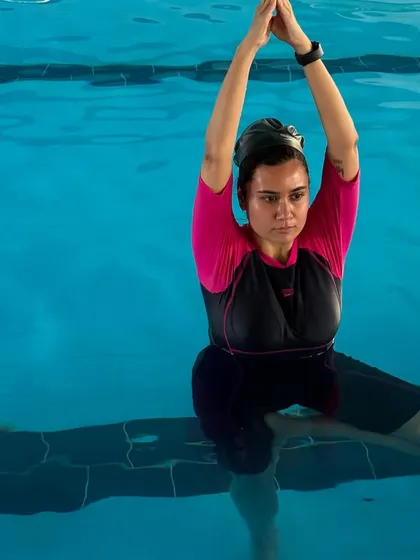 A participant practices a seated overhead stretch in the pool. The water provides gentle resistance, which helps to build strength while stretching.