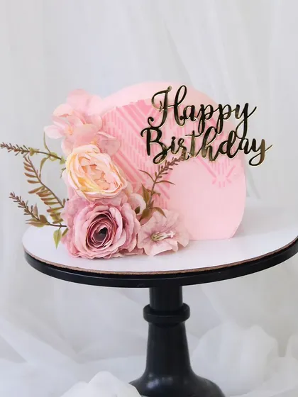 A beautiful pastel pink cake with a subtle textured finish. This elegant design is adorned with a simple arrangement of silk flowers, making it perfect for a sophisticated birthday celebration.