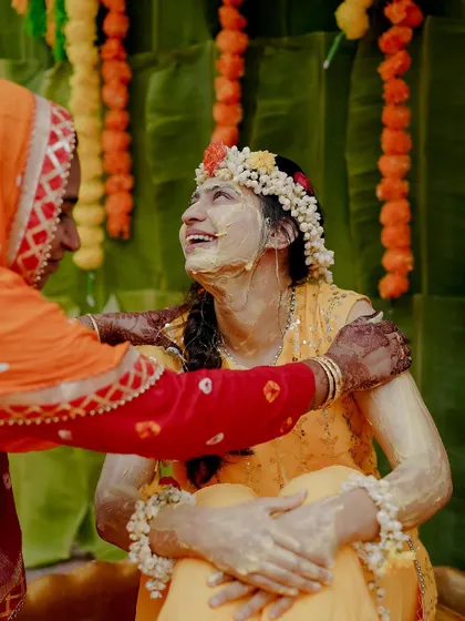 The bride looking up with a smile, surrounded by family during her Haldi. This photo captures a moment of happiness and anticipation.
