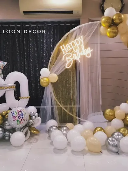 A sophisticated setup for a 20th birthday, featuring a gold and white balloon semi-arch, a neon sign, and a custom balloon bouquet.