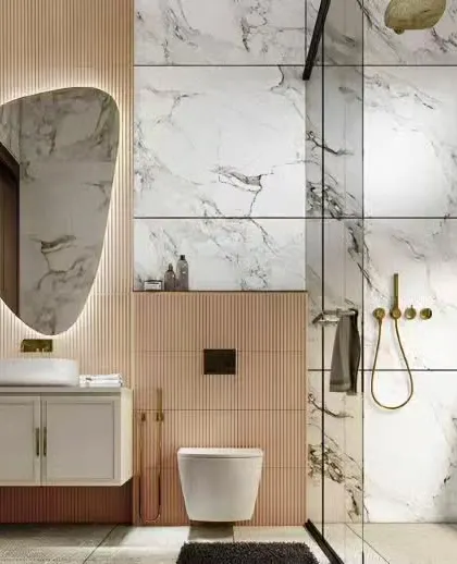 This bathroom exudes luxury with floor-to-ceiling marble-patterned tiles and rose gold fixtures. The organic-shaped backlit mirror adds a soft, contemporary touch.