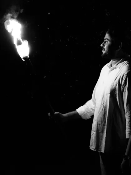 A black and white profile shot of the groom-to-be holding a flaming torch. The focus is on his silhouette and the intense light from the fire, adding a dramatic flair to the couple's photoshoot series.