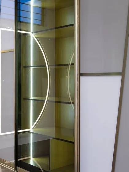 This close-up reveals the detail of the sliding wardrobe's construction. The combination of grey, white, and tinted glass panels with integrated lighting creates a sophisticated and highly custom look.