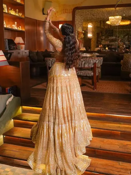 A golden hour glow for this bride. Her hair is styled in a half-up braid with flowing waves, perfectly complementing her shimmering lehenga.