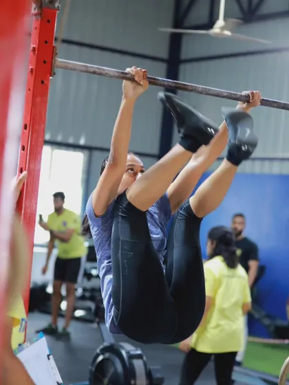 A female athlete performs a toes-to-bar during a competition. This gymnastic movement is a staple in CrossFit-style events and requires significant core strength and coordination.
