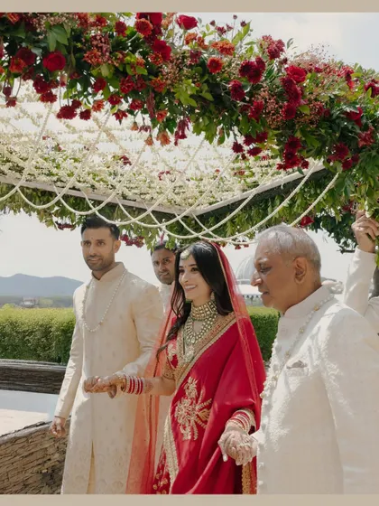 The bride, Nikita, being escorted to the mandap by her family. The floral canopy above adds a touch of natural beauty to this important procession.