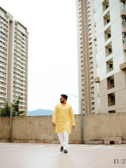 A stylish shot of the groom walking in his Haldi outfit, with modern buildings in the background creating a cool urban contrast.
