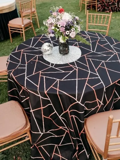 A stylish table setting from a K-Pop themed party. The black tablecloth with a geometric rose gold pattern, combined with a disco ball centerpiece, creates a chic and modern look.