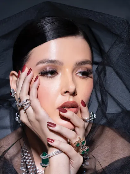 A pensive and dramatic portrait. The model's pose and the dark veil create a moody atmosphere that makes the diamond and emerald jewelry appear even more brilliant.