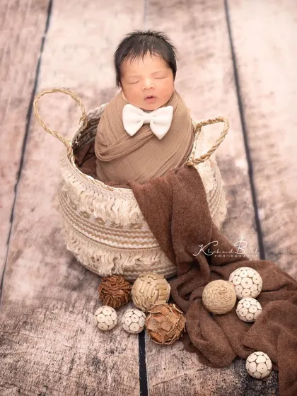 A little gentleman in the making. This newborn looks dapper with a tiny white bow tie, nestled in a rustic basket on a wooden floor.