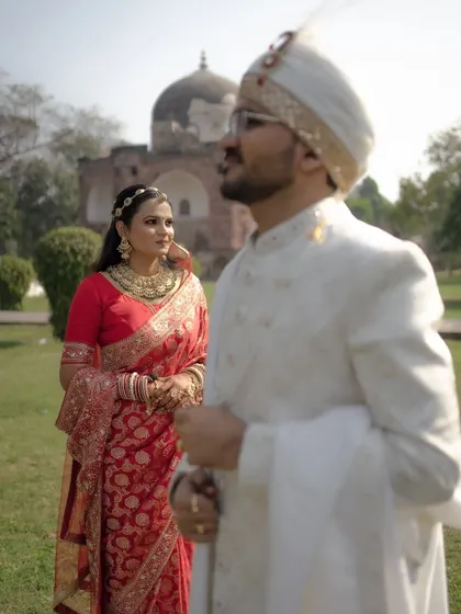 A beautifully composed shot with the bride in sharp focus, looking towards her groom who is softly blurred in the foreground, set against a historic monument.