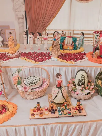 An angled view of Kajal's baby shower, showing the extensive doll setup, food baskets, and decorative items that filled the corner of the hall.
