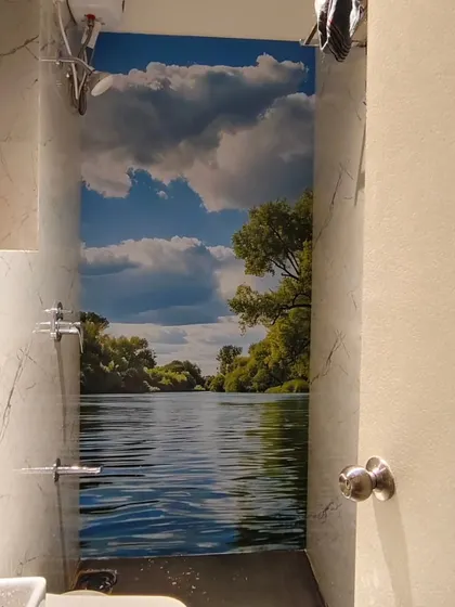 Another example of a peel-and-stick wallpaper installed on bathroom tiles, this time with a serene river scene.