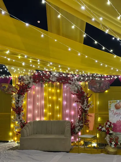 The main seating area for the terrace Haldi. A simple sofa is placed in front of a circular floral arch and a backdrop of pink and yellow drapes with fairy lights.