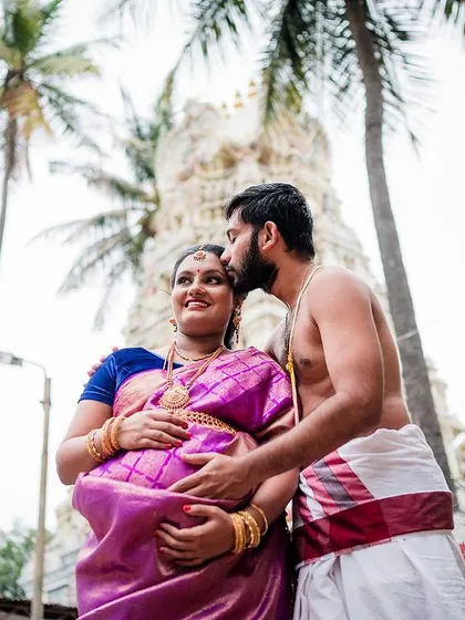 A tender moment with the husband-to-be kissing his wife's forehead during their outdoor maternity shoot, with a temple in the background.