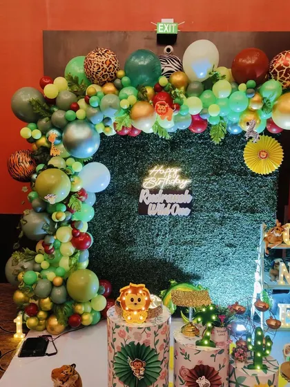 This "Wild One" birthday setup uses a grass wall backdrop, a neon sign, and a balloon arch with leopard print accents for a modern safari look.