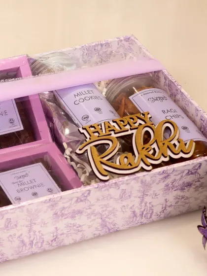 A close up of the packaging for our healthy Rakhi hamper, showing the 'Happy Rakhi' tag and the Dior inspired print.