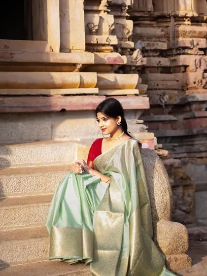 Seated on the steps of a temple in a soft green Banarasi saree. The warm sunlight and relaxed posture create a moment of calm and connection with the sacred space.