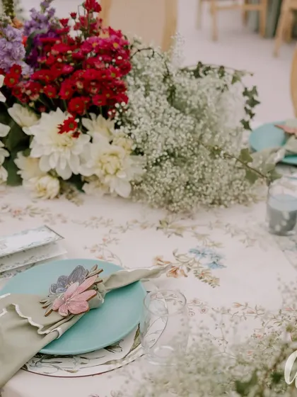 A close-up of the table setting, showing the floral-print linen, custom laser-cut napkin rings, and a mix of dahlias and baby's breath. These details are essential for a luxurious feel.