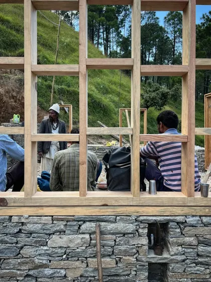 A moment of rest for the construction crew, framed by a newly installed window structure. The work is physically demanding, and the skill of these craftsmen is what brings the architectural vision to life.