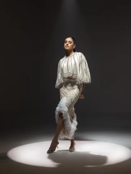 The full look of the ivory cape and skirt ensemble, captured in a spotlight to emphasize its dramatic and couture feel.