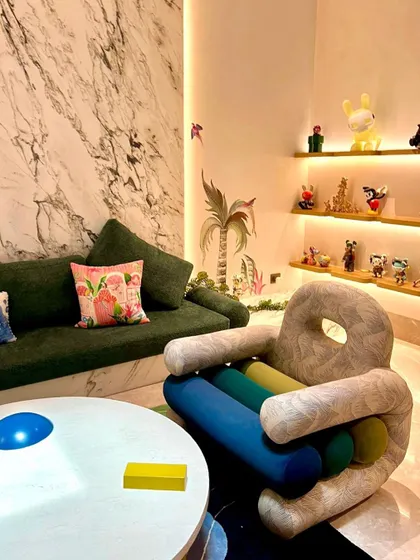 Here you can see the details of the custom armchair's textured upholstery and the deep green built-in sofa. The backlit shelves display a collection of designer toys, adding a personal and whimsical touch to this postmodern living space.