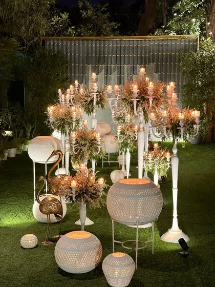 A whimsical installation of white candelabras, lanterns, and golden flamingo statues on the lawn.