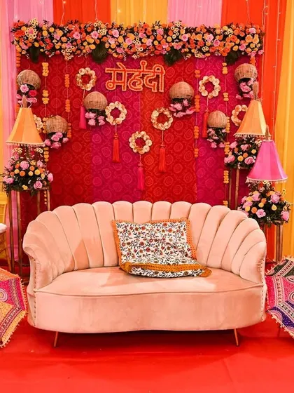 A classic mehendi seating setup with a vibrant pink and yellow backdrop, traditional Rajasthani umbrellas, and a plush velvet sofa.