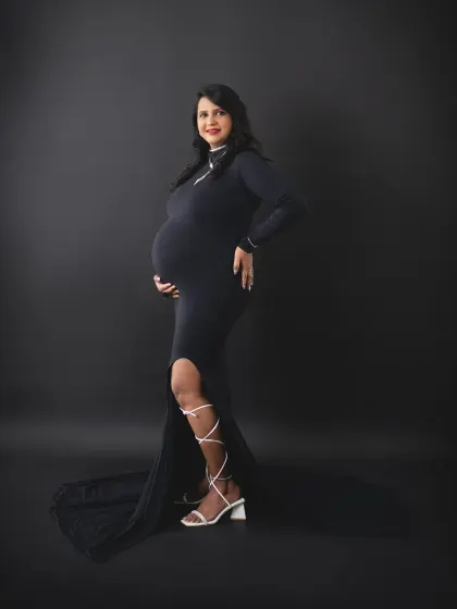 A full-length portrait of a mom-to-be looking absolutely glamorous in a fitted black gown and strappy heels. A perfect choice for a stylish, modern maternity shoot.