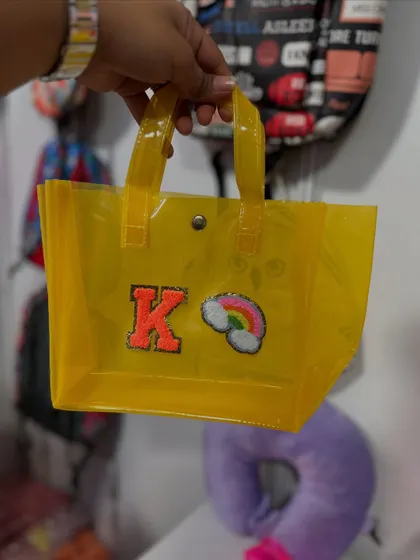 A small, transparent yellow tote bag personalized with an initial and a rainbow patch. These are perfect for carrying small items in style.