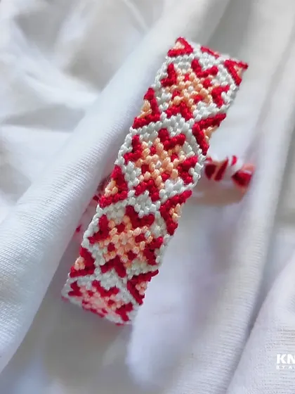 This friendship bracelet features a lovely star or flower-like pattern in shades of red, pink, and white.