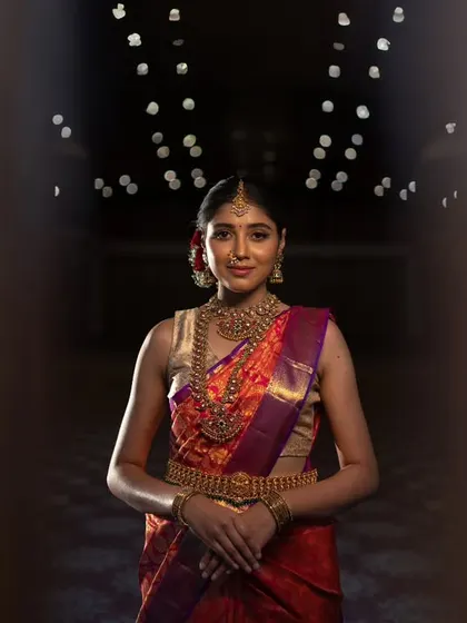 A classic portrait of a South Indian bride, her beauty and traditional attire framed in a doorway. The bokeh lights in the background add a touch of sparkle.