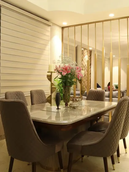 This dining space features a beige palette with a sleek marble table and a striking gold-finished metal partition that separates it from the living area.