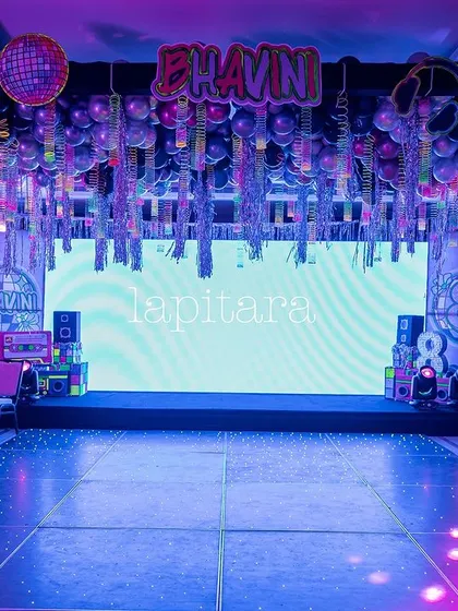 The main stage and dance floor of a neon glow party, with a large LED screen and a ceiling dripping with shimmering tinsel.