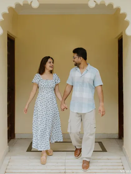A happy, walking shot of the couple holding hands in a corridor with classic Indian architecture.