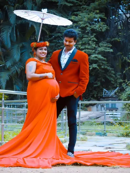 A lovely outdoor portrait of an expecting couple, with the man in a red blazer that perfectly matches his partner's red trail gown.