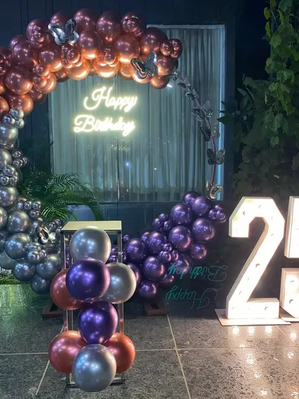 A stylish 25th birthday outdoor setup with a balloon ring in metallic shades of purple, silver, and rose gold.