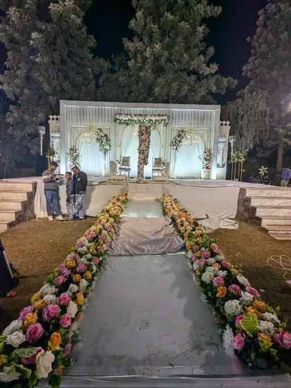 A grand Nikah stage setup with a long floral-lined aisle. The stage features a beautiful partition made of hanging flower strings, creating a dramatic focal point.