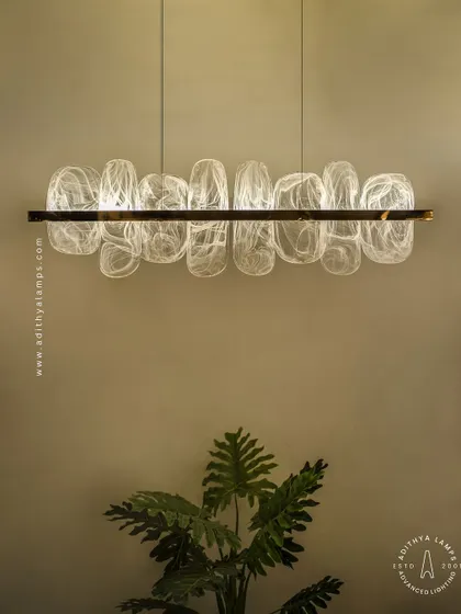This linear pendant features organic, rounded glass elements with a beautiful white smoke effect inside. Suspended from a simple gold bar, it provides a soft, ethereal glow, ideal for creating a serene atmosphere over a dining table.